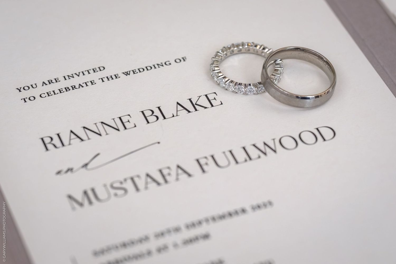 Close-up view of wedding rings and elegant invitation details printed on luxurious white paper.