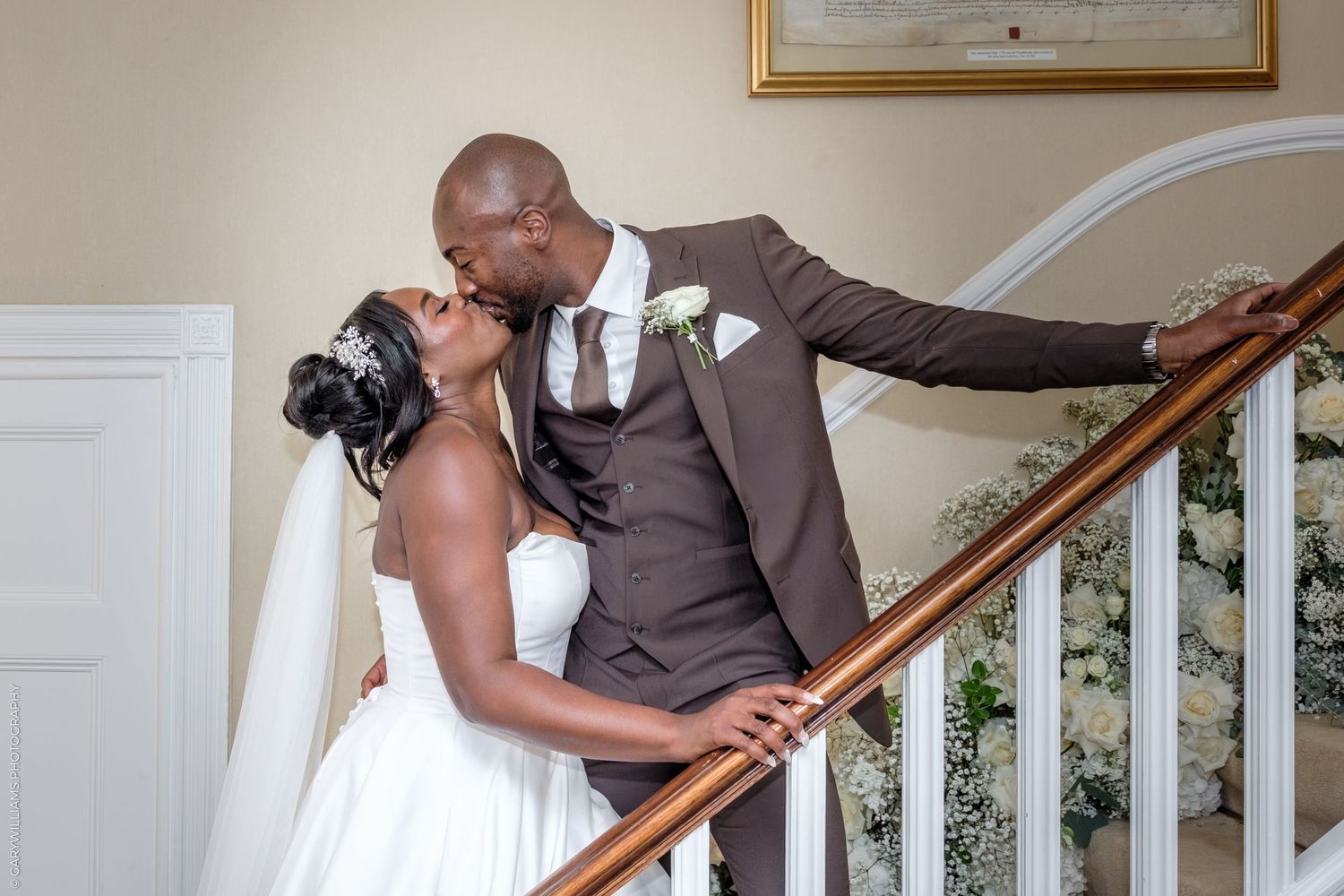 A couple in formal wedding attire share a romantic kiss while posing on an elegant staircase.
