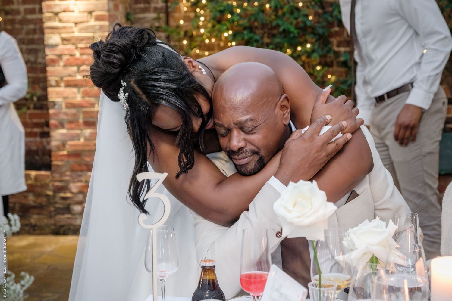 A tender moment shared between a couple at their wedding reception table decorated with white flowers and candles.