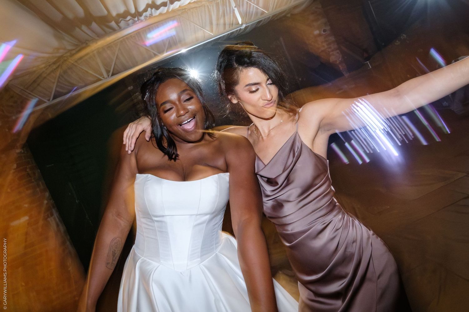 Two people in formal attire share an intimate dance moment at a dimly lit wedding reception venue.