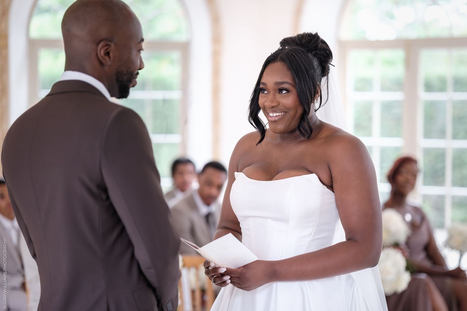 Elegant wedding ceremony in a bright indoor venue with arched windows and white decor.