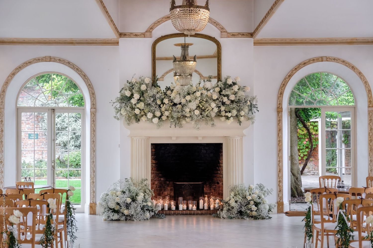 Elegant white wedding venue interior with arched windows, floral arrangements, and natural lighting.