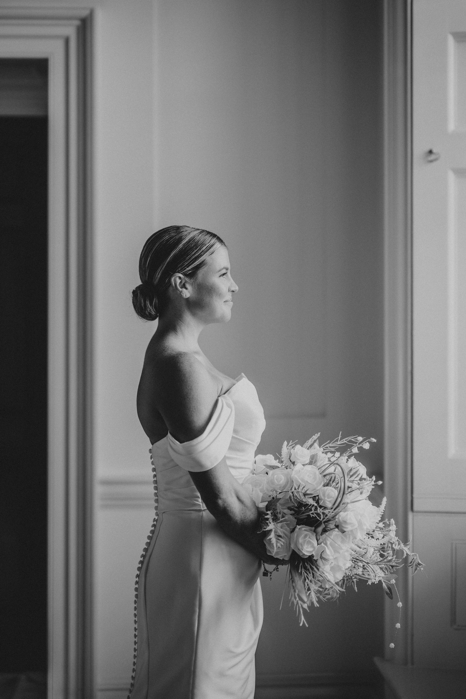 Black and white series showing a person in white dress holding a floral bouquet while looking out a window.