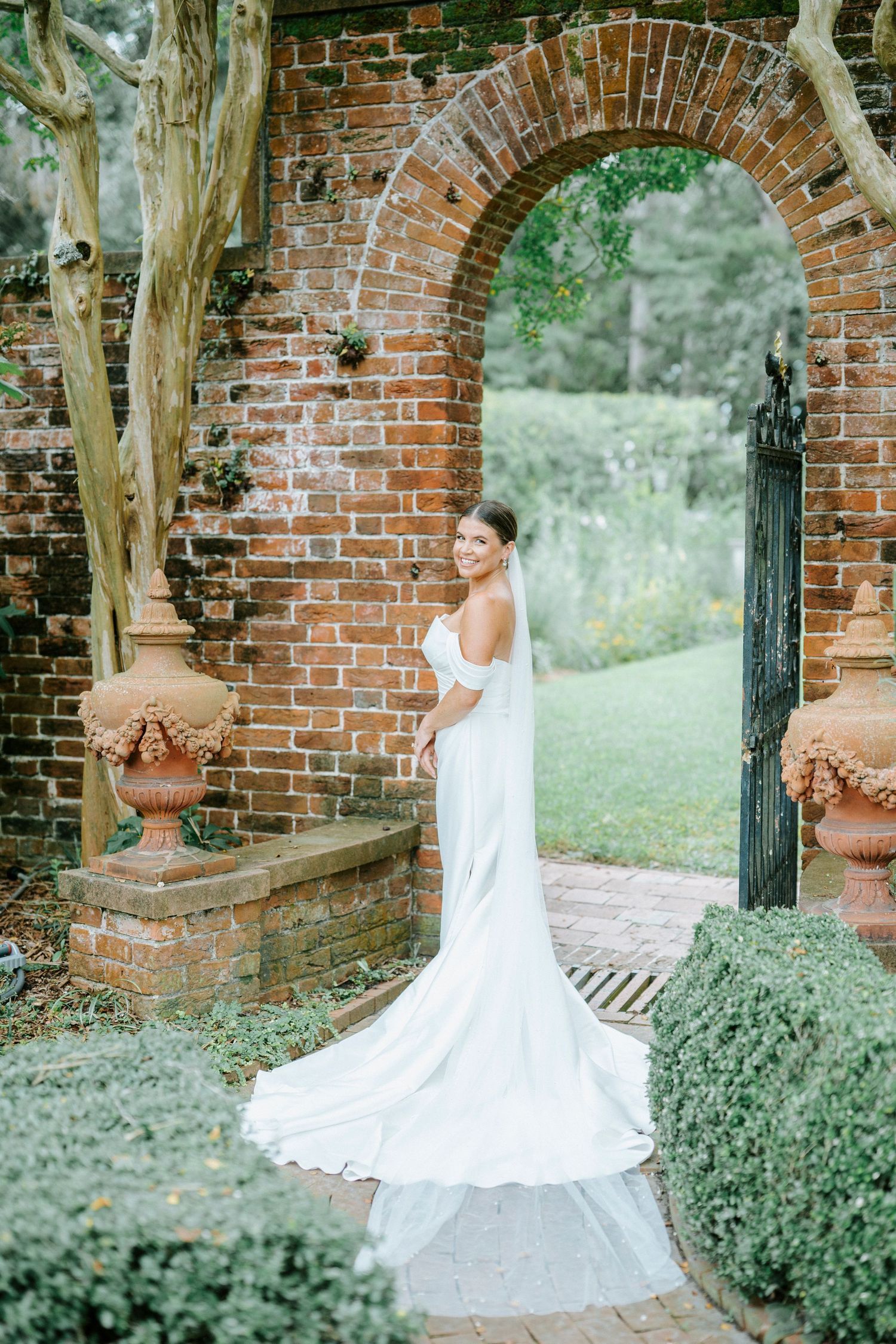 A bride in a flowing white wedding dress twirls gracefully among rustic brick archways and lush greenery.