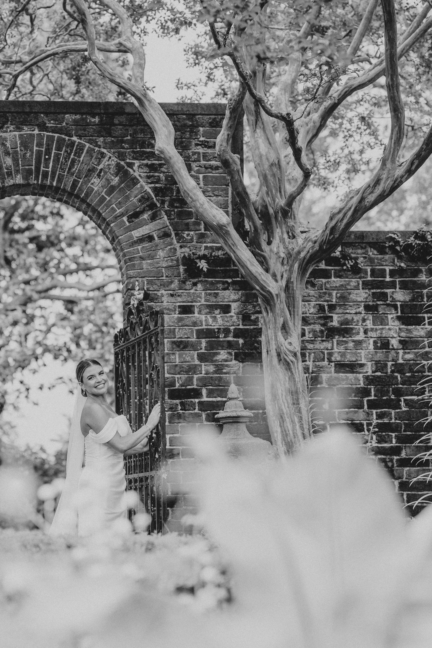 A black and white series of photos showing a person in white against a brick wall with tree branches overhead.