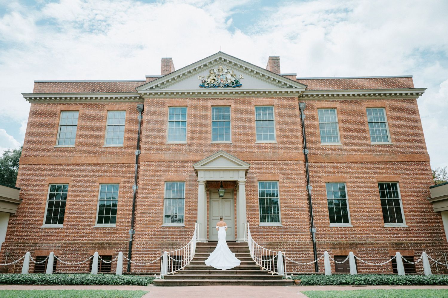 A panoramic view of a symmetrical Georgian-style brick mansion with white columns and grand entrance steps.