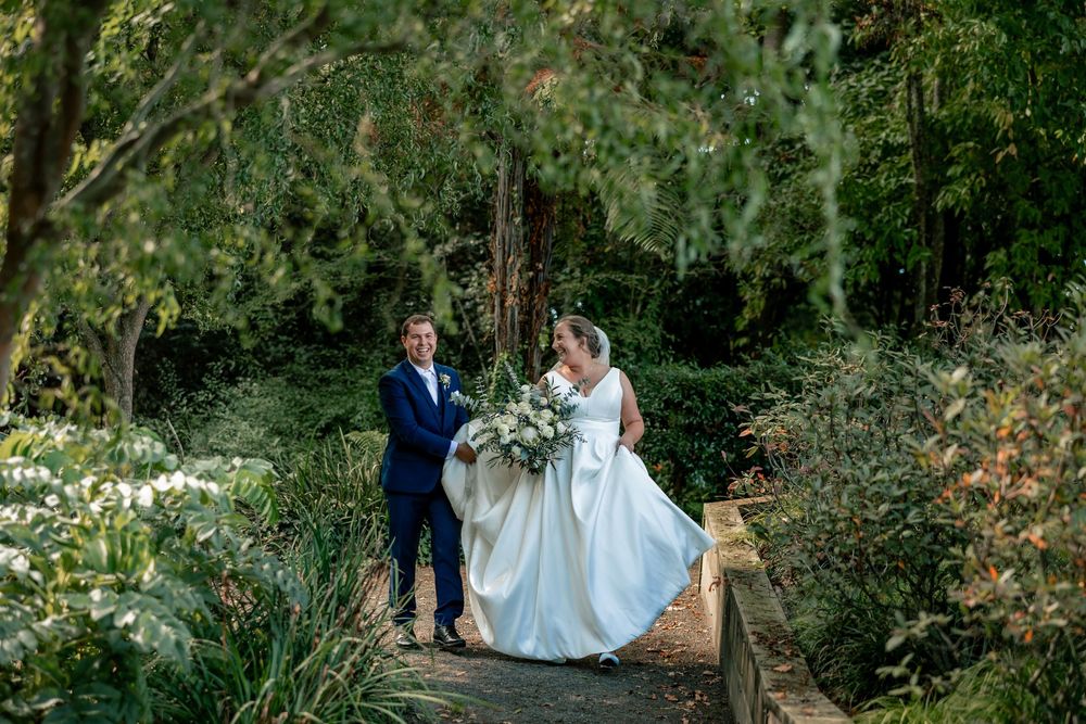 A couple in wedding attire walks through a lush garden path surrounded by greenery on their special day.