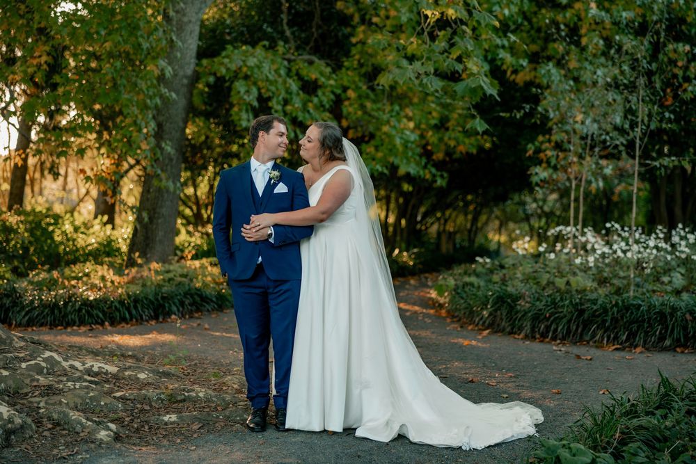 Bride and groom pose together outdoors in a garden setting during golden hour with lush greenery.