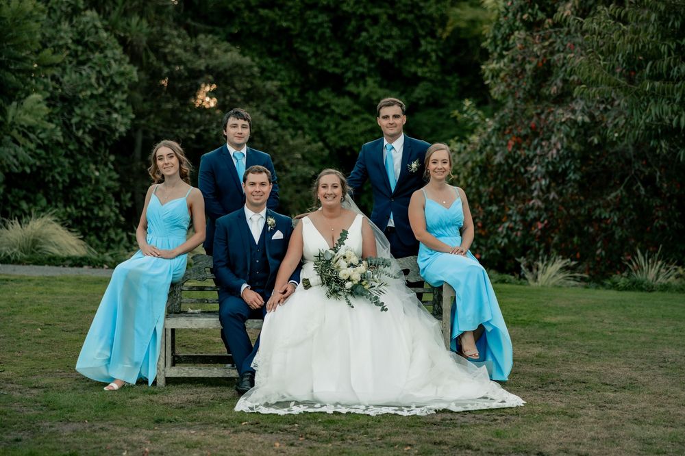 Wedding party in light blue dresses and navy suits poses together on a green lawn at Woodlands estate Hamilton NZ