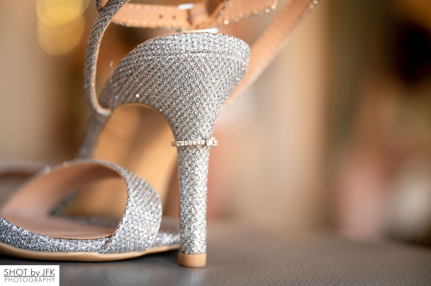 Close-up view of a silver glittery high heel sandal with rhinestone embellishments against a blurred background.