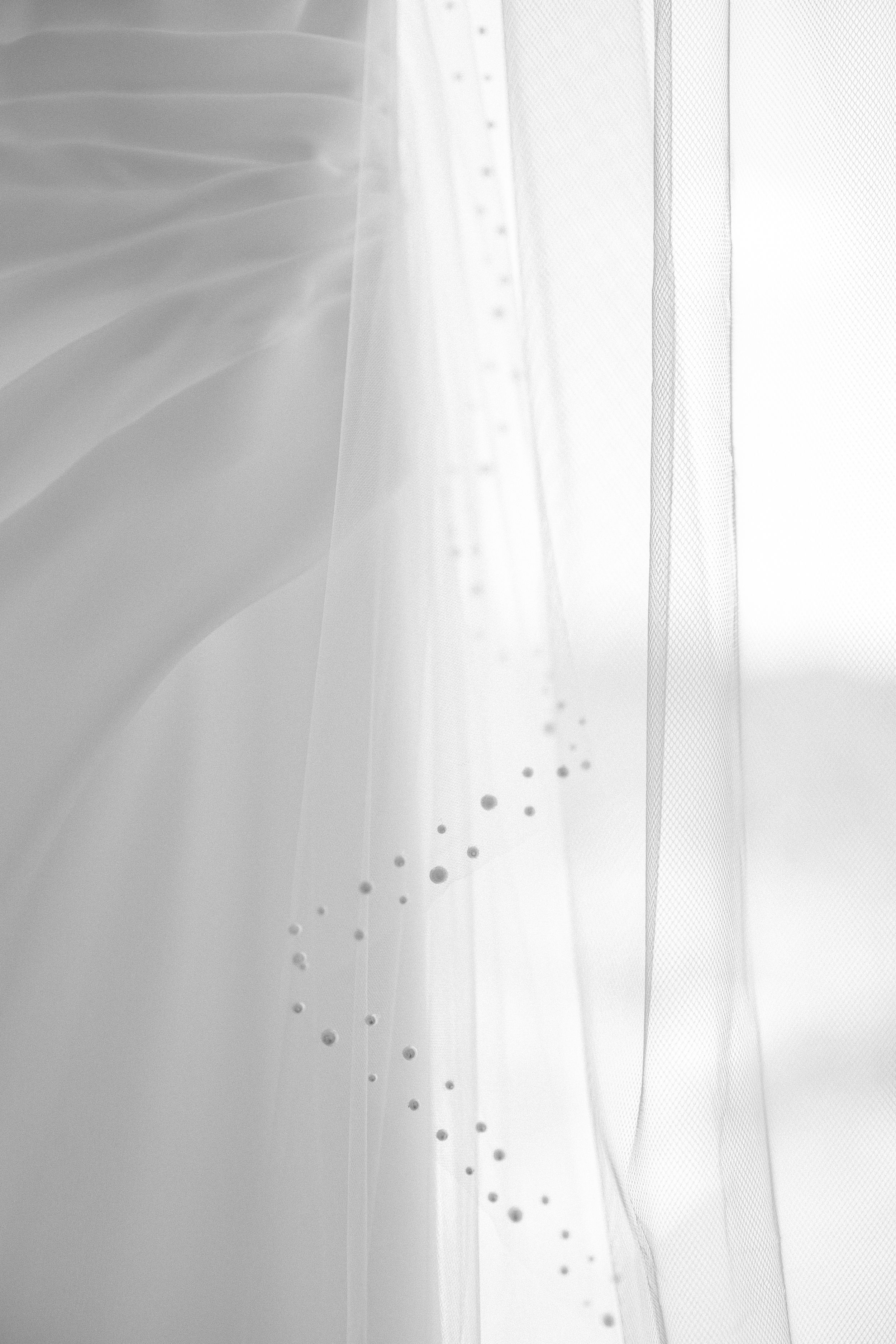 Ethereal white sheer curtains with delicate dotted pattern filtering soft natural light through a window.