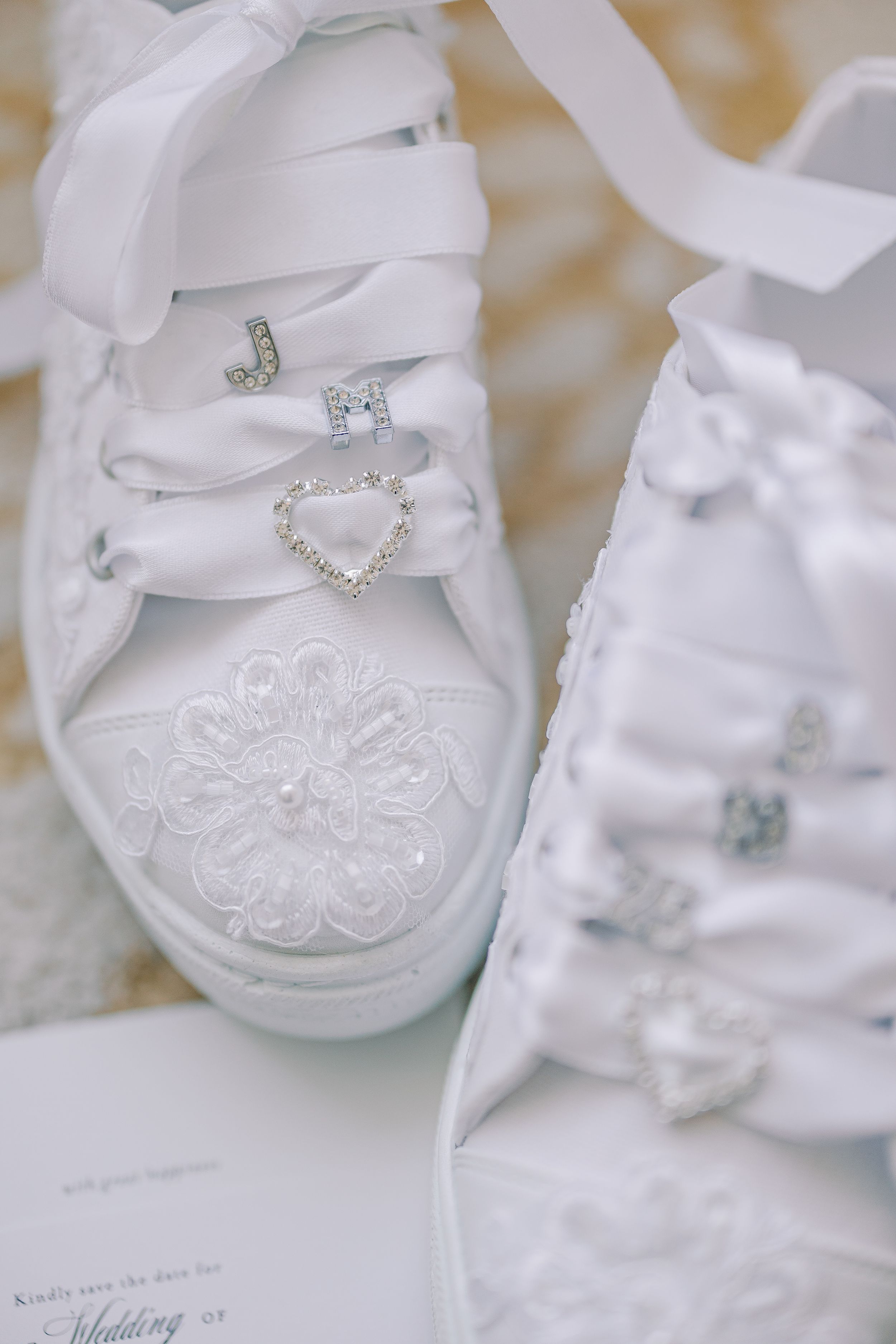 Elegant white wedding shoes adorned with ornate lace details and crystal embellishments on a light surface.