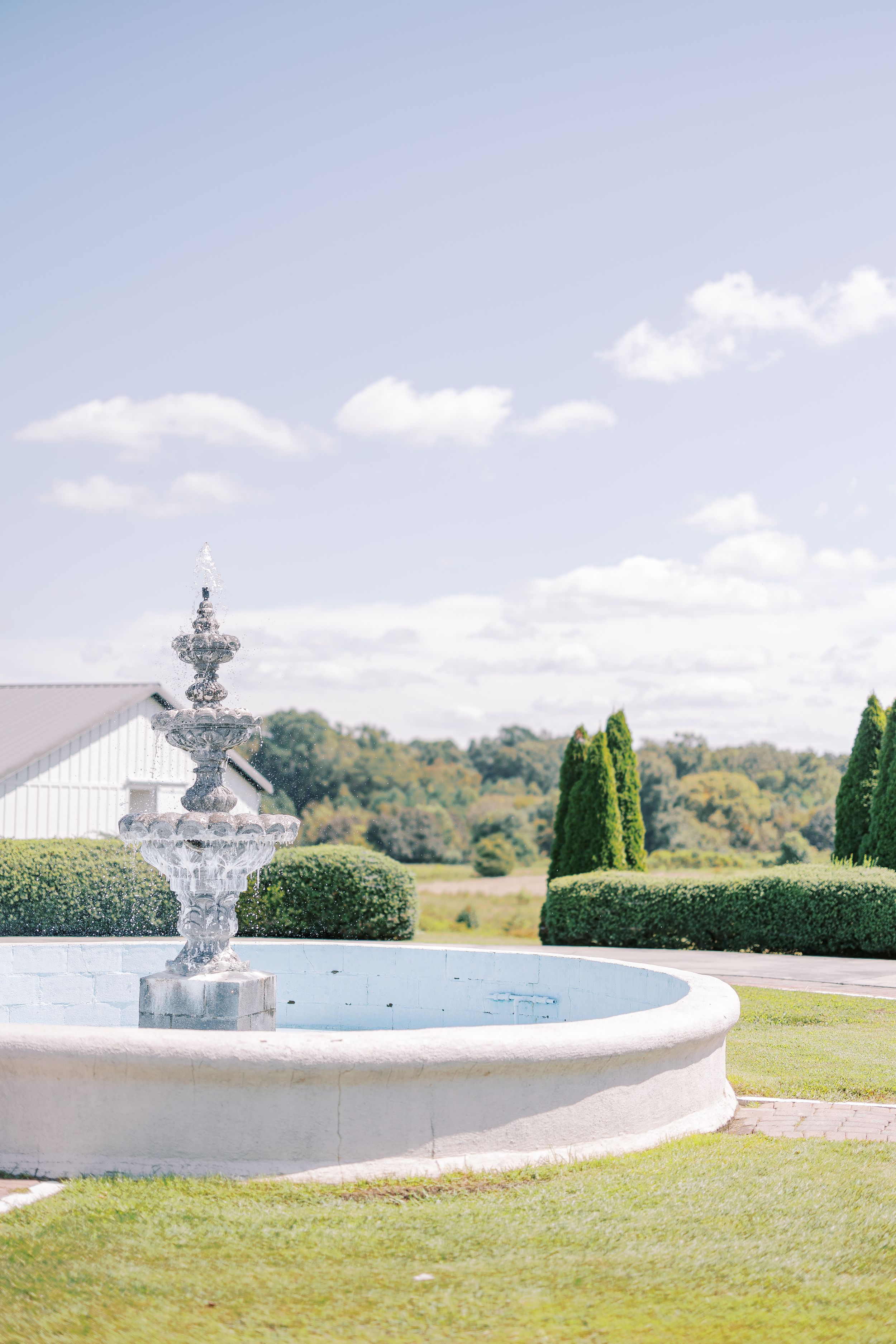 White stone retaining wall curves around a manicured lawn against a bright blue sky with puffy clouds.