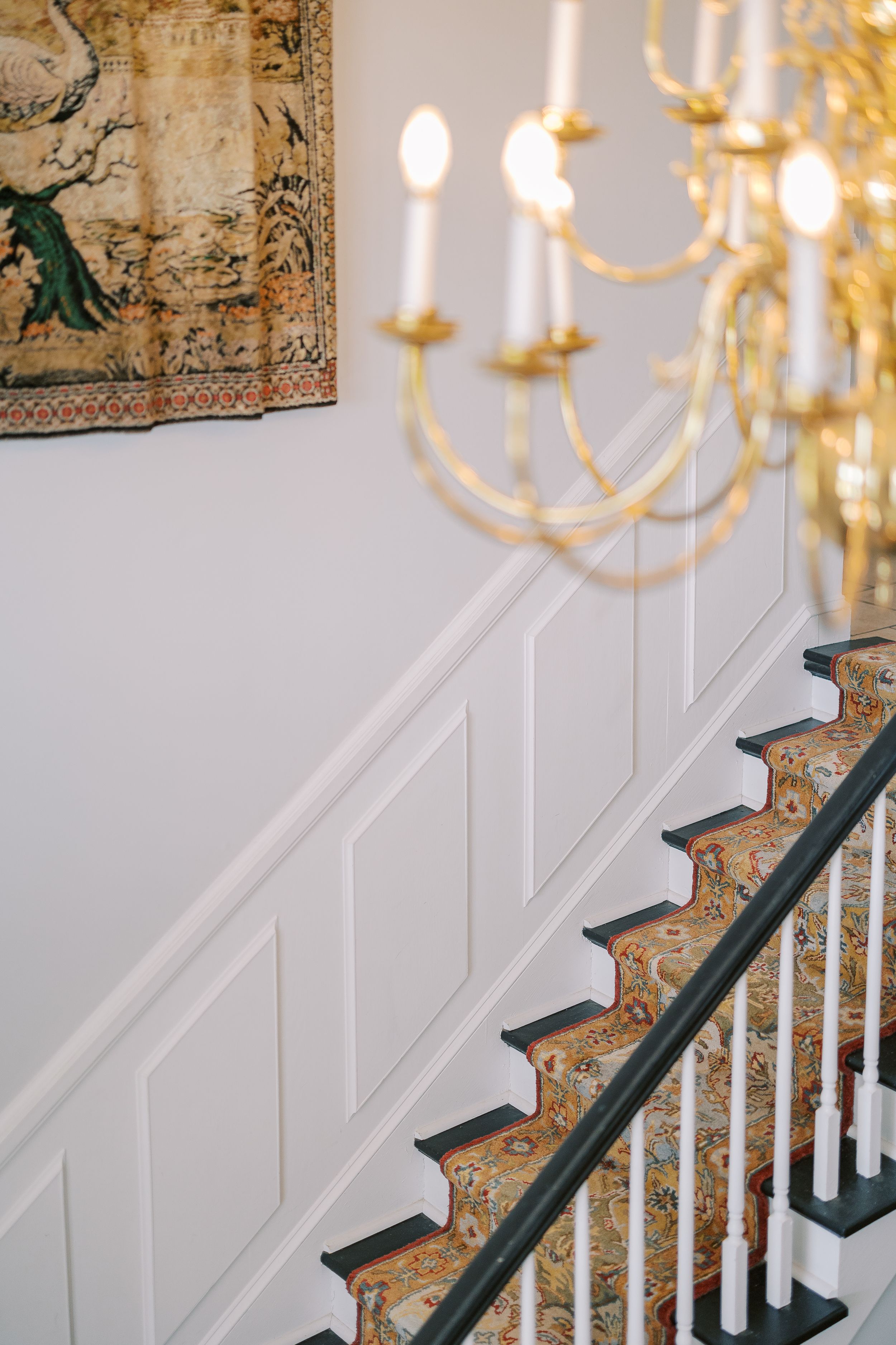 Elegant curved staircase with white wainscoting and ornate gold chandelier in classic interior setting.