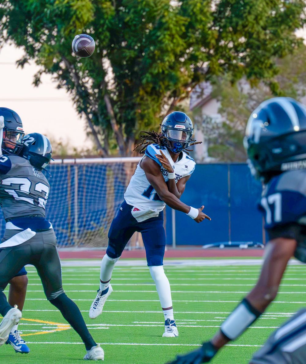 High school quarterback in white uniform throws a pass under pressure during a football game.