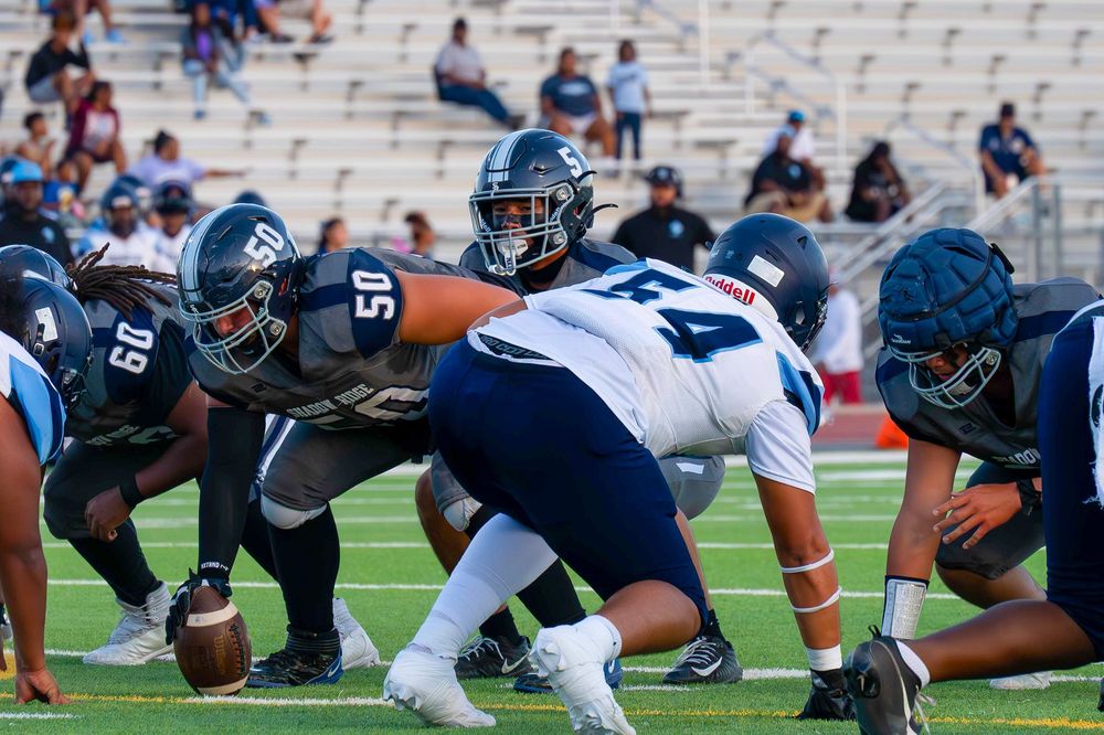 Football players in navy and gray uniforms face off at the line of scrimmage during a daytime game.