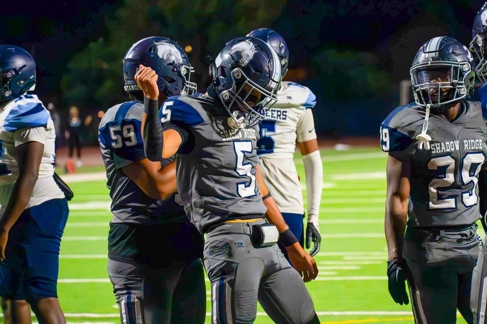 High school football players #59 and #5 celebrate on the field during a night game.