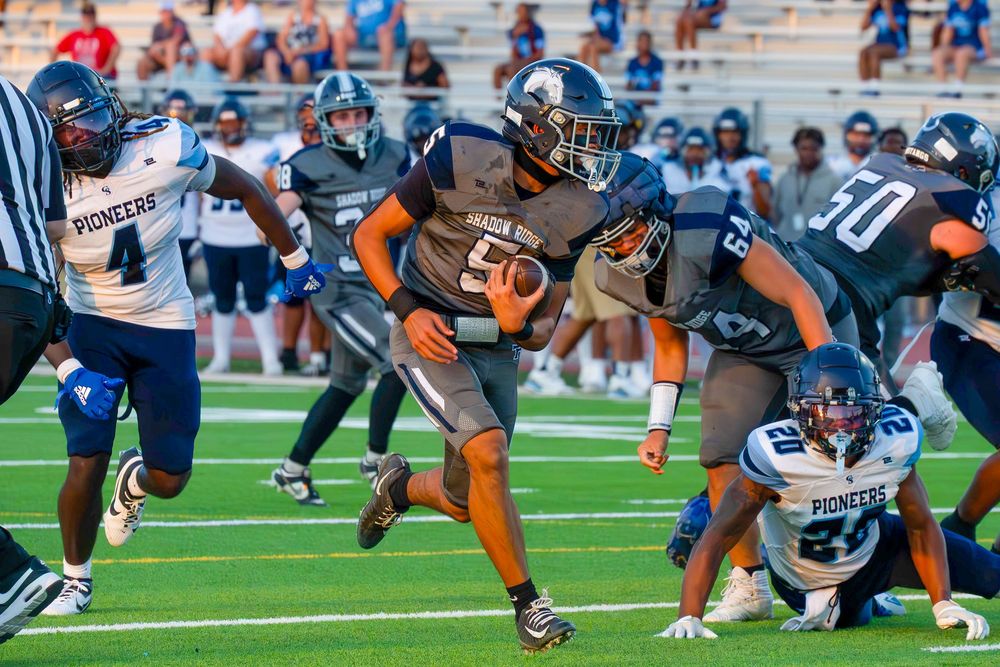 Football player number 50 in orange and gray uniform runs through a gap against Pioneers defenders.