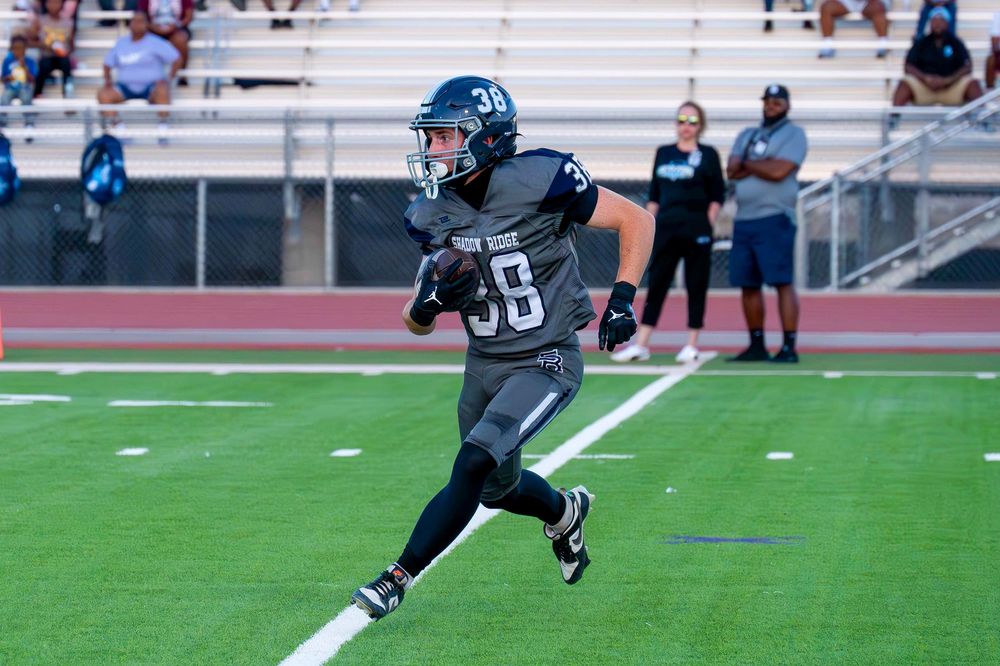 Football player #55 in gray uniform runs with the ball during a high school game.