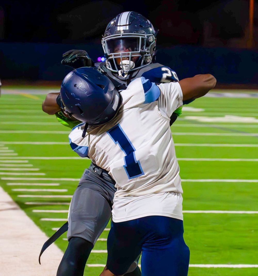 Two football players compete for the ball during a night game, one in white jersey making a catch.