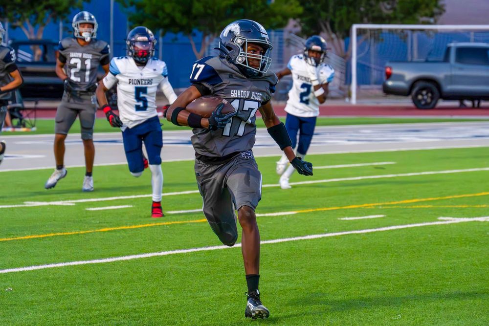 Football player number 17 in gray uniform sprints toward the end zone past blue-jersyed defenders.