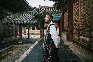 Tourist explores traditional Korean architecture with wooden buildings and ornate roofs at dusk.