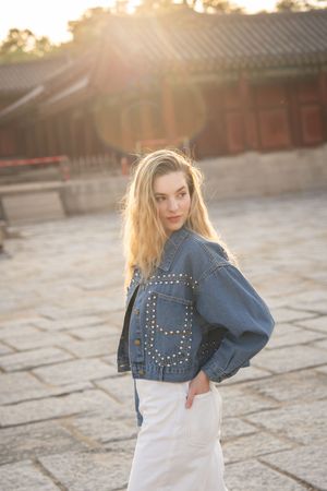 Woman in denim jacket posing against traditional Korean palace buildings at sunset.