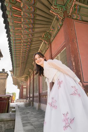 White hanbok dress with pink cherry blossom details photographed in a palace corridor.
