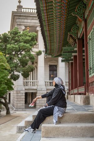 Person resting along a covered walkway with ornate traditional Korean architectural details.