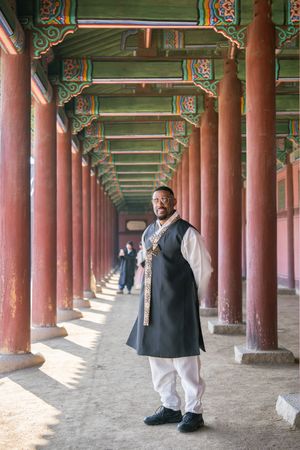 Historic Korean palace colonnade with red pillars and decorated green ceiling beams.