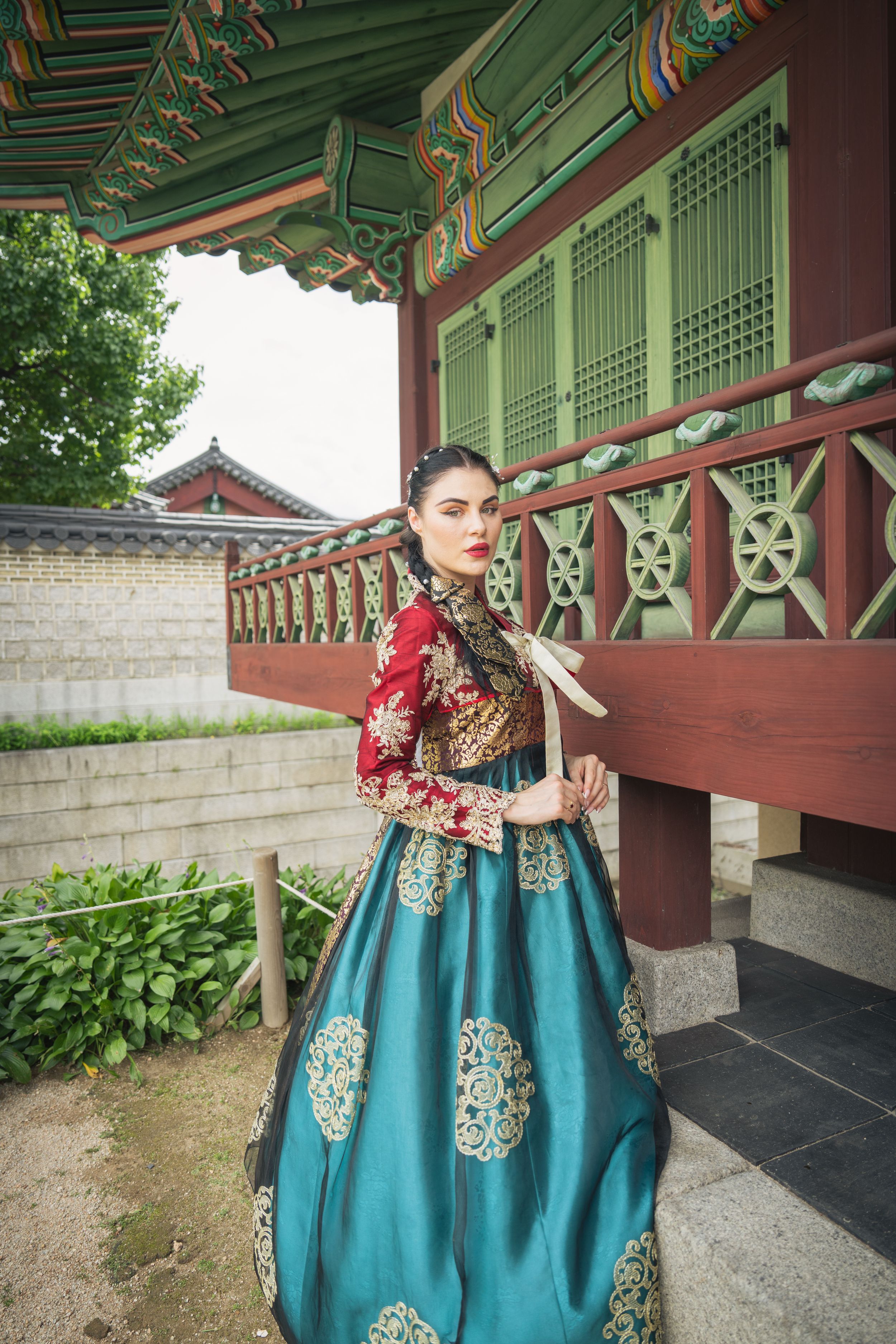 Person in a turquoise and gold hanbok dress posing along a traditional Korean palace corridor.