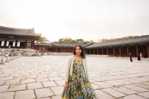 Person in a summery floral dress explores a traditional Korean courtyard with stone pathways.
