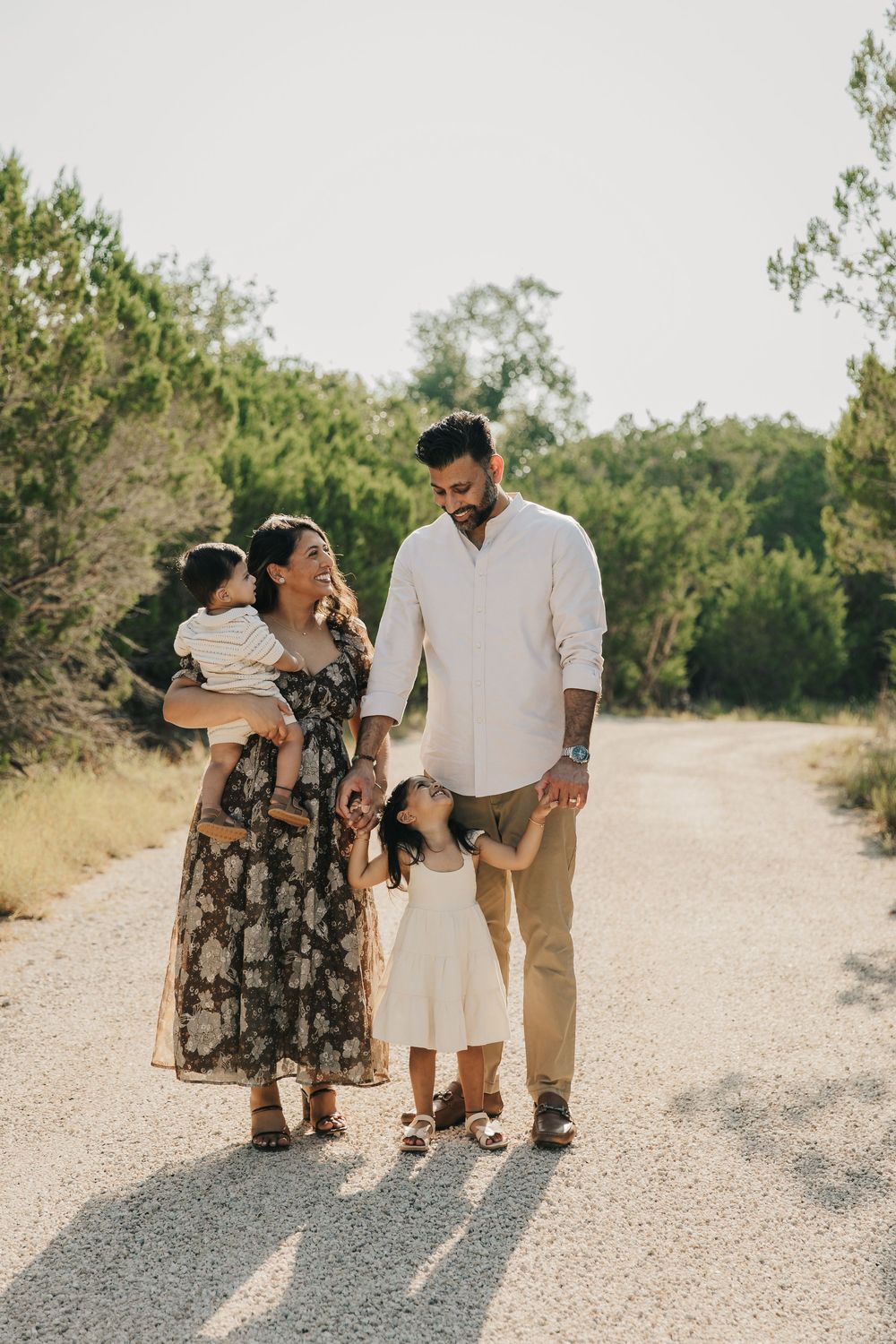 A family enjoys a sunny walk together on a gravel path surrounded by green foliage.