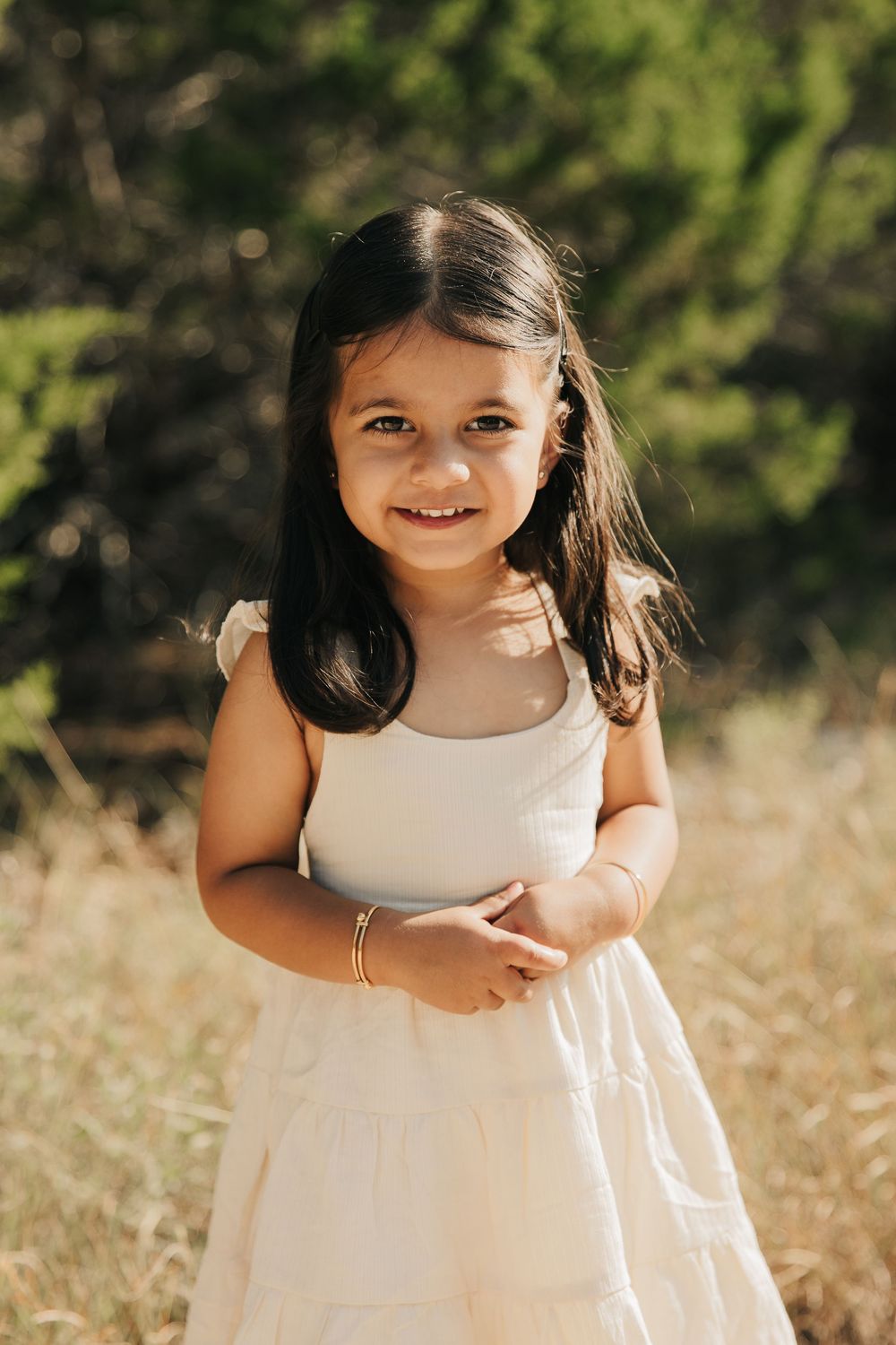 A child in a white dress enjoying a sunny afternoon in a grassy meadow with golden sunlight filtering through trees.