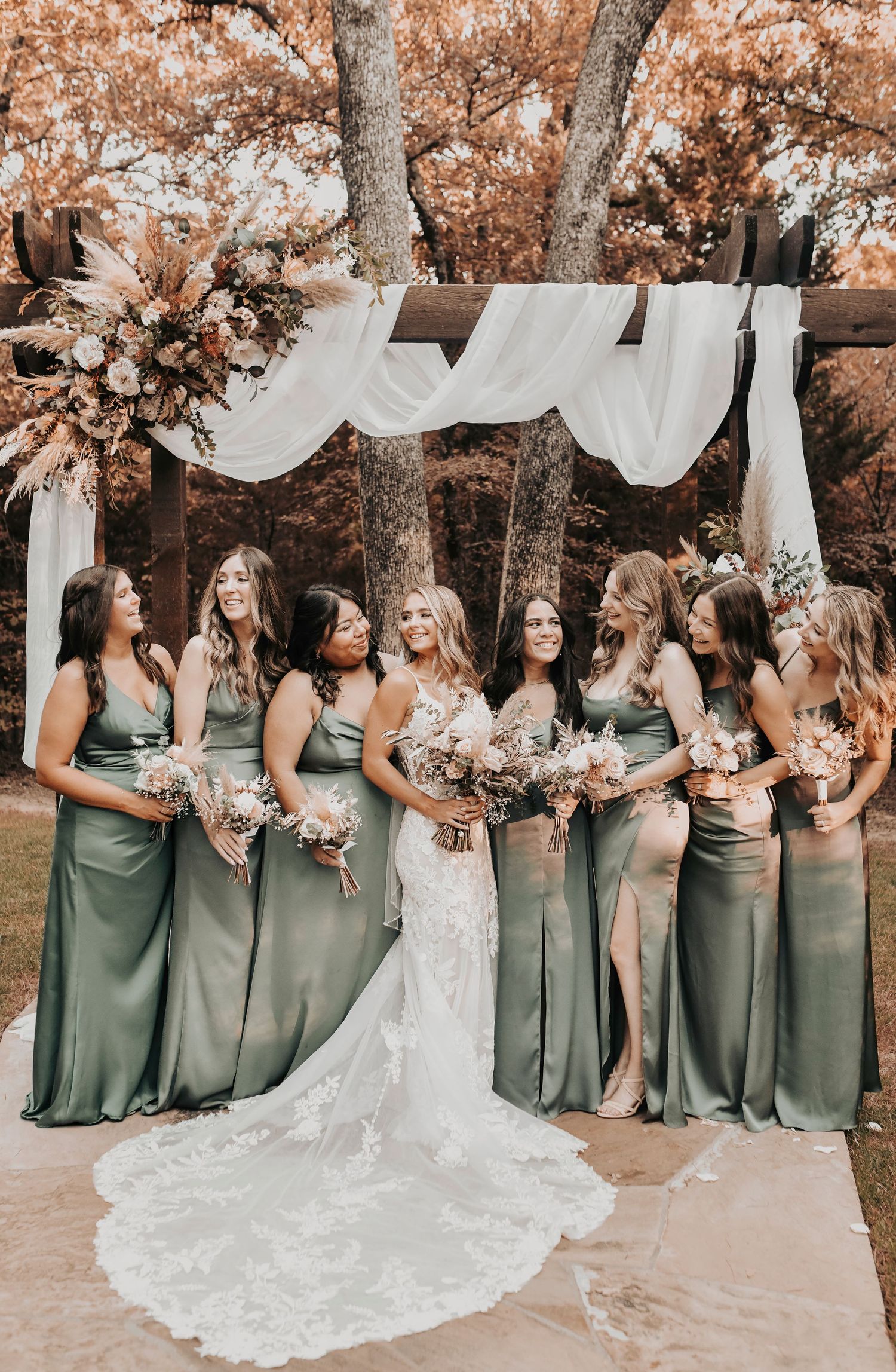 Bridesmaids in olive green dresses holding boho earth-tone bouquets with bride in lace gown