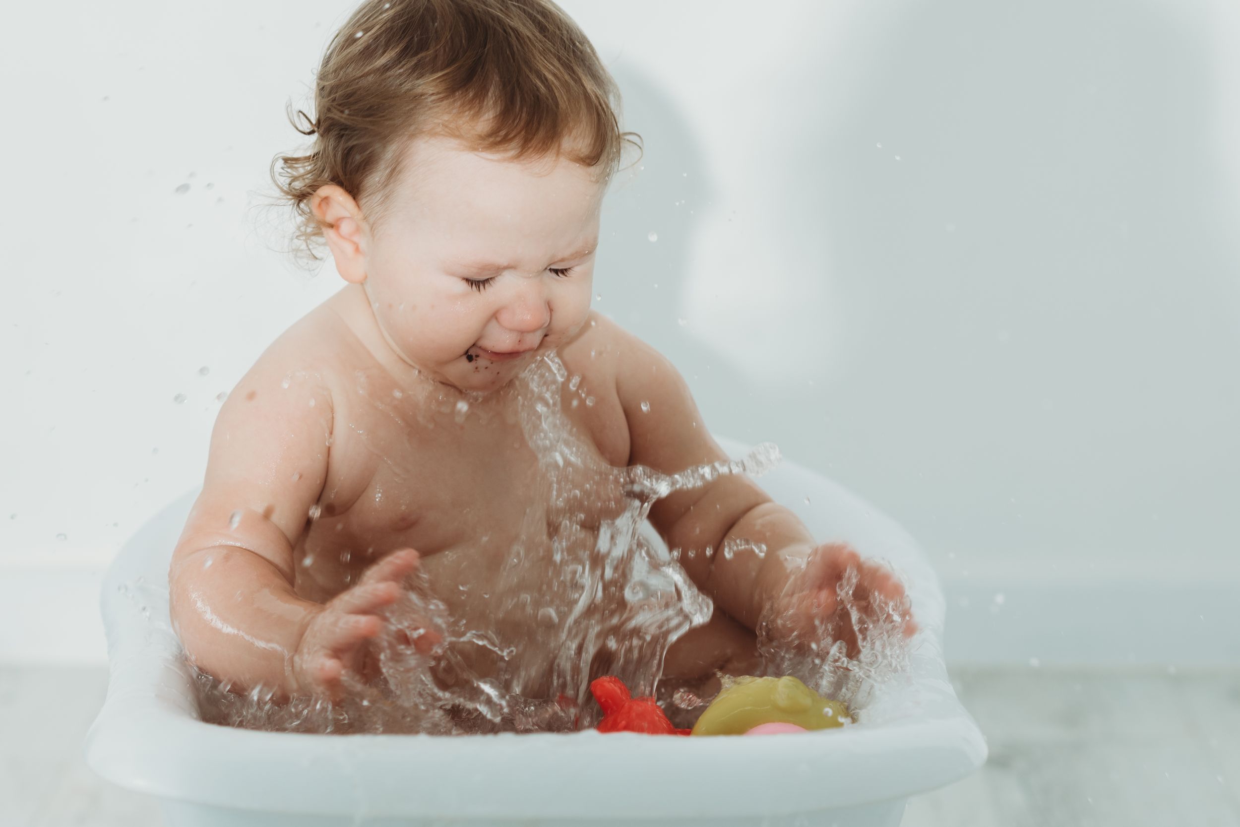Baby splashing and playing with toys during bathtime with water droplets flying.