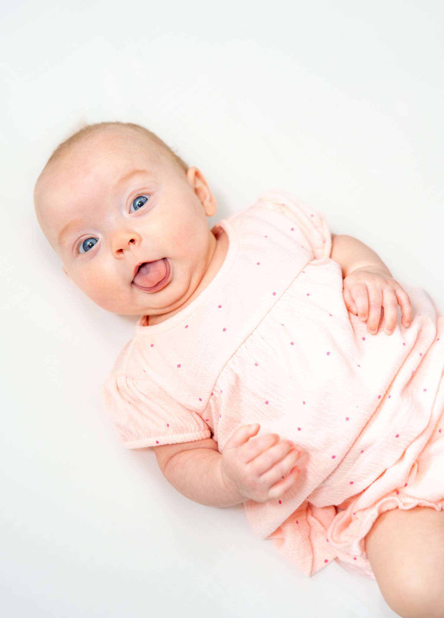 Baby wearing light pink outfit showing four different playful expressions against white background. Quad Cities Newborn Photography