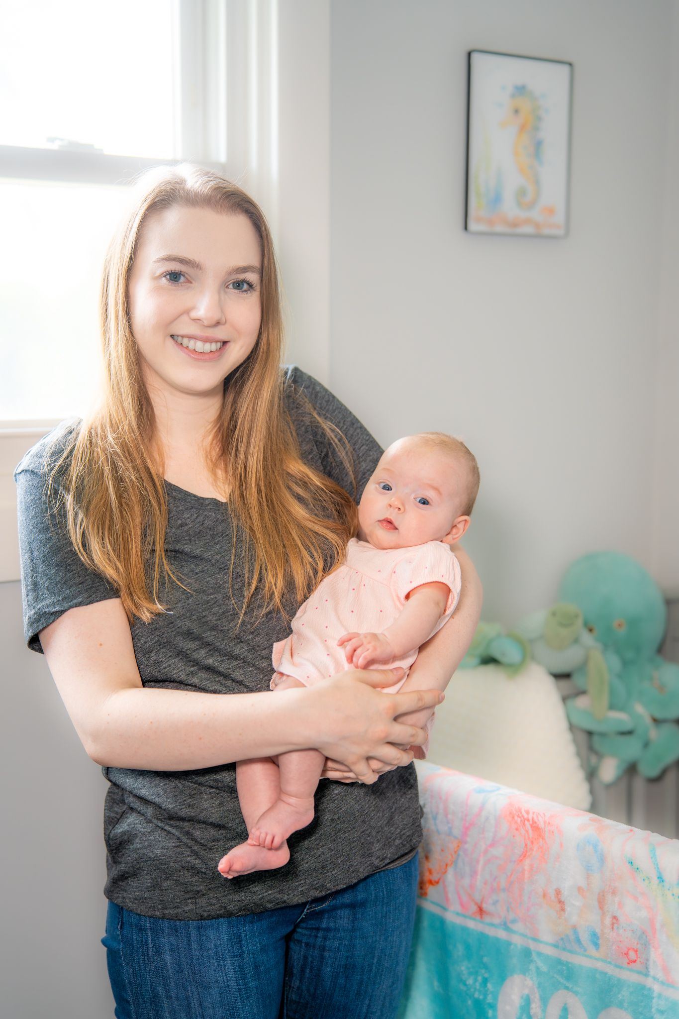 A young mother holds a baby wearing pink in a nursery decorated with aqua and coral colors. Quad Cities Newborn Photography