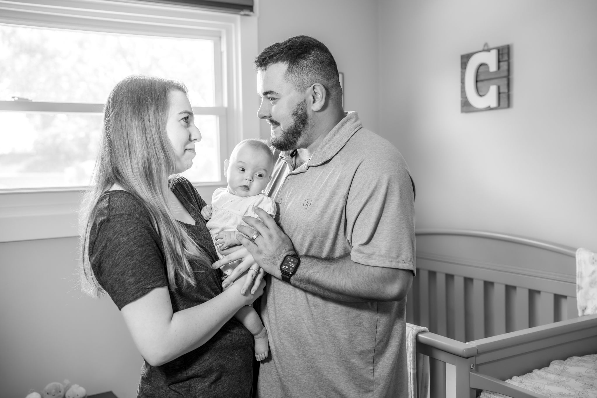 A tender scene unfolds as someone stands close to a baby in a crib in a dimly lit nursery. Quad Cities Newborn Photography