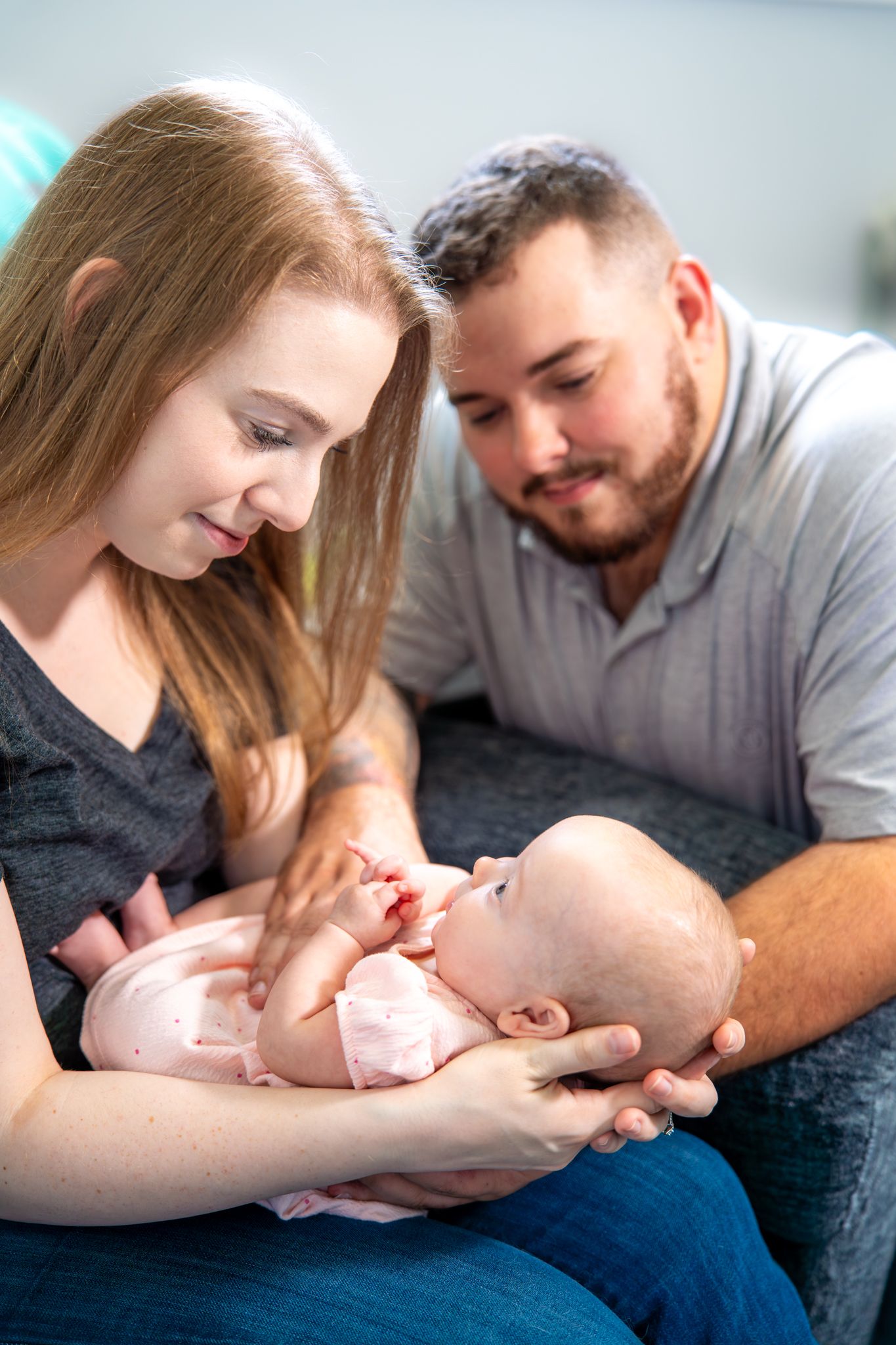 Parents lovingly bonding with their newborn baby while relaxing on a cozy couch at home. Quad Cities Newborn Photography