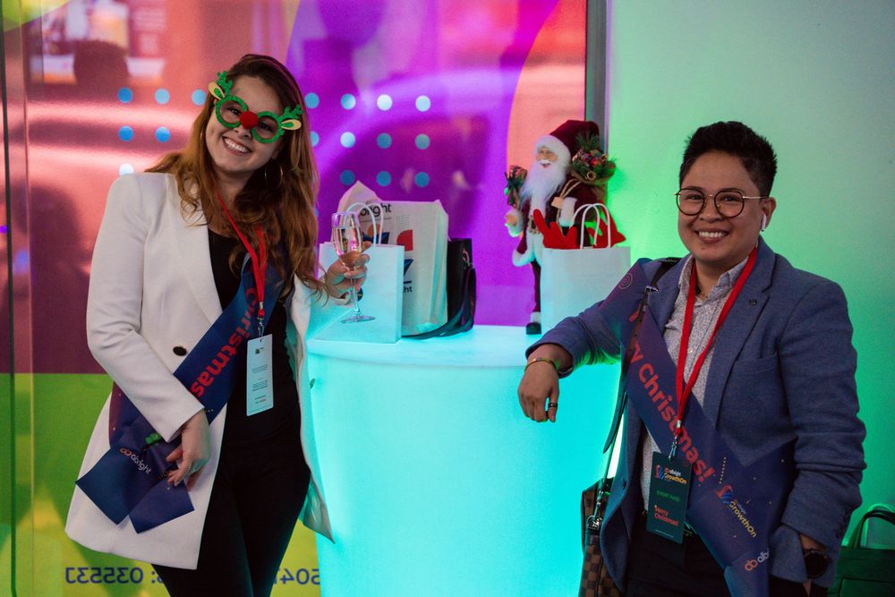 Groups of people interact at a social networking event with colorful purple and blue lighting in the background.