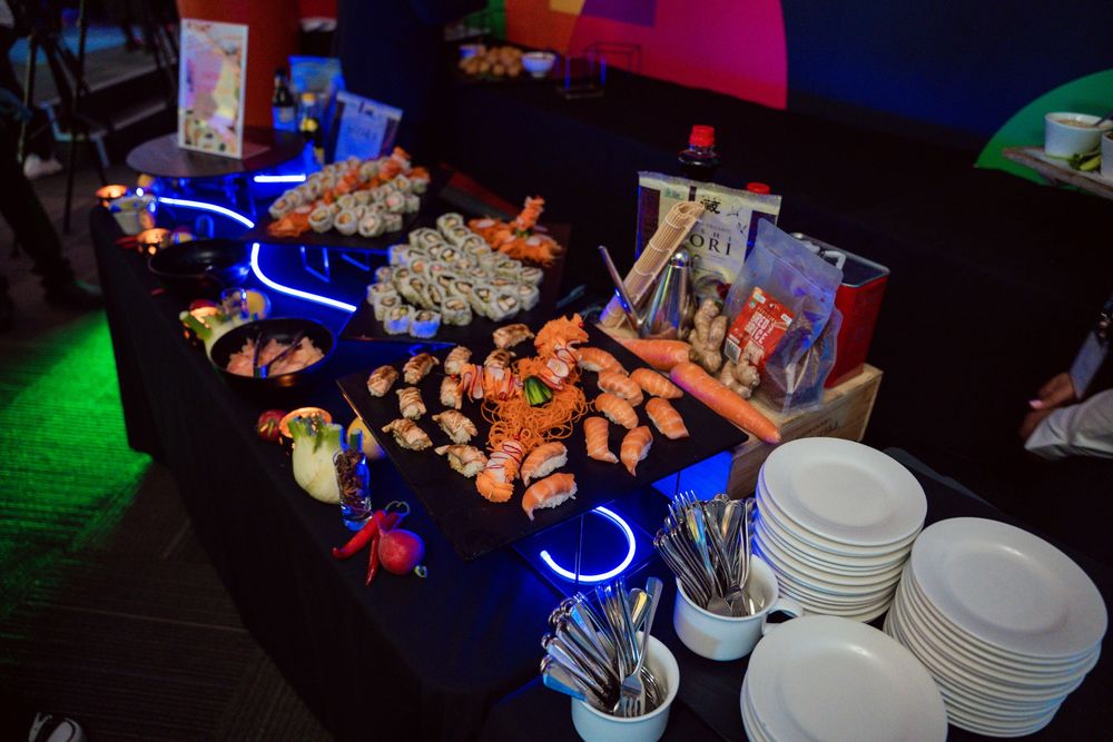 A buffet table illuminated with blue LED lights displays various snacks, appetizers, and white plates for serving.