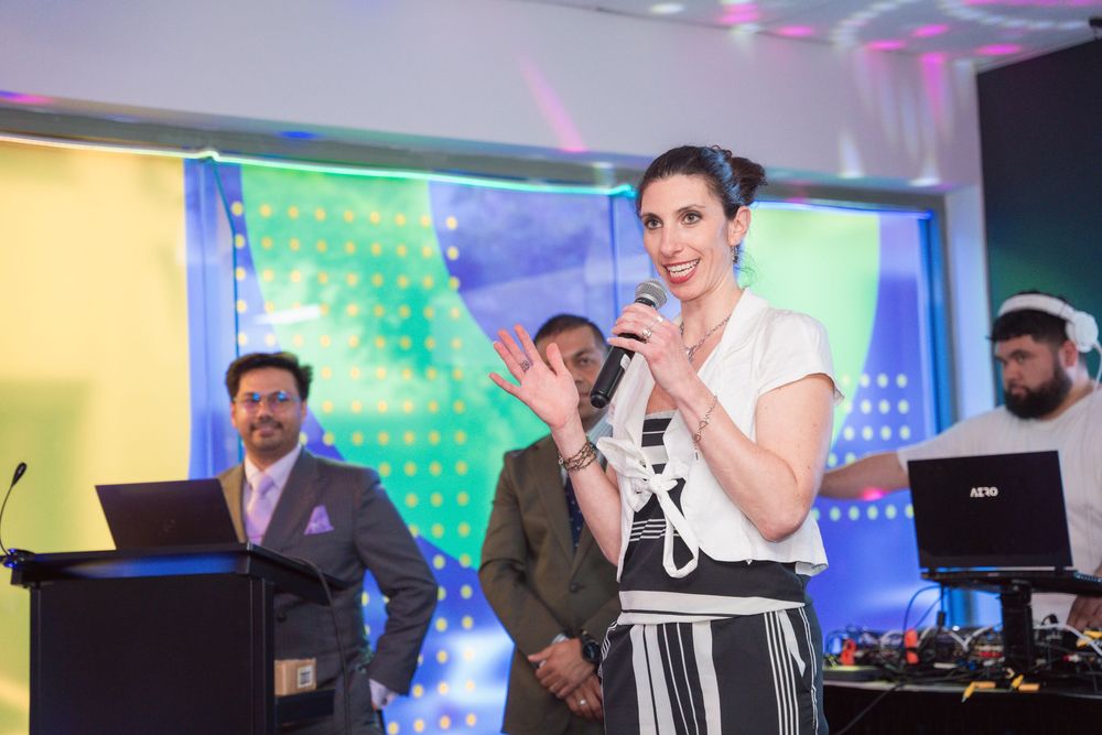 Speaker presenting at a tech event with colorful backdrop and audio equipment.