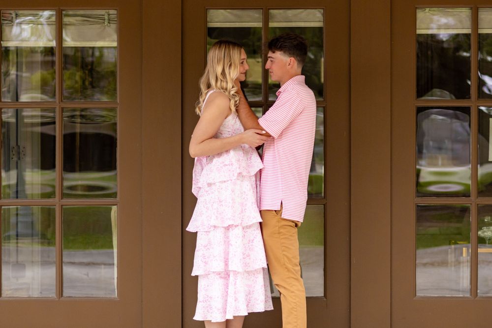 Couple in coordinating pink outfits standing face to face in front of elegant glass doors outdoors.