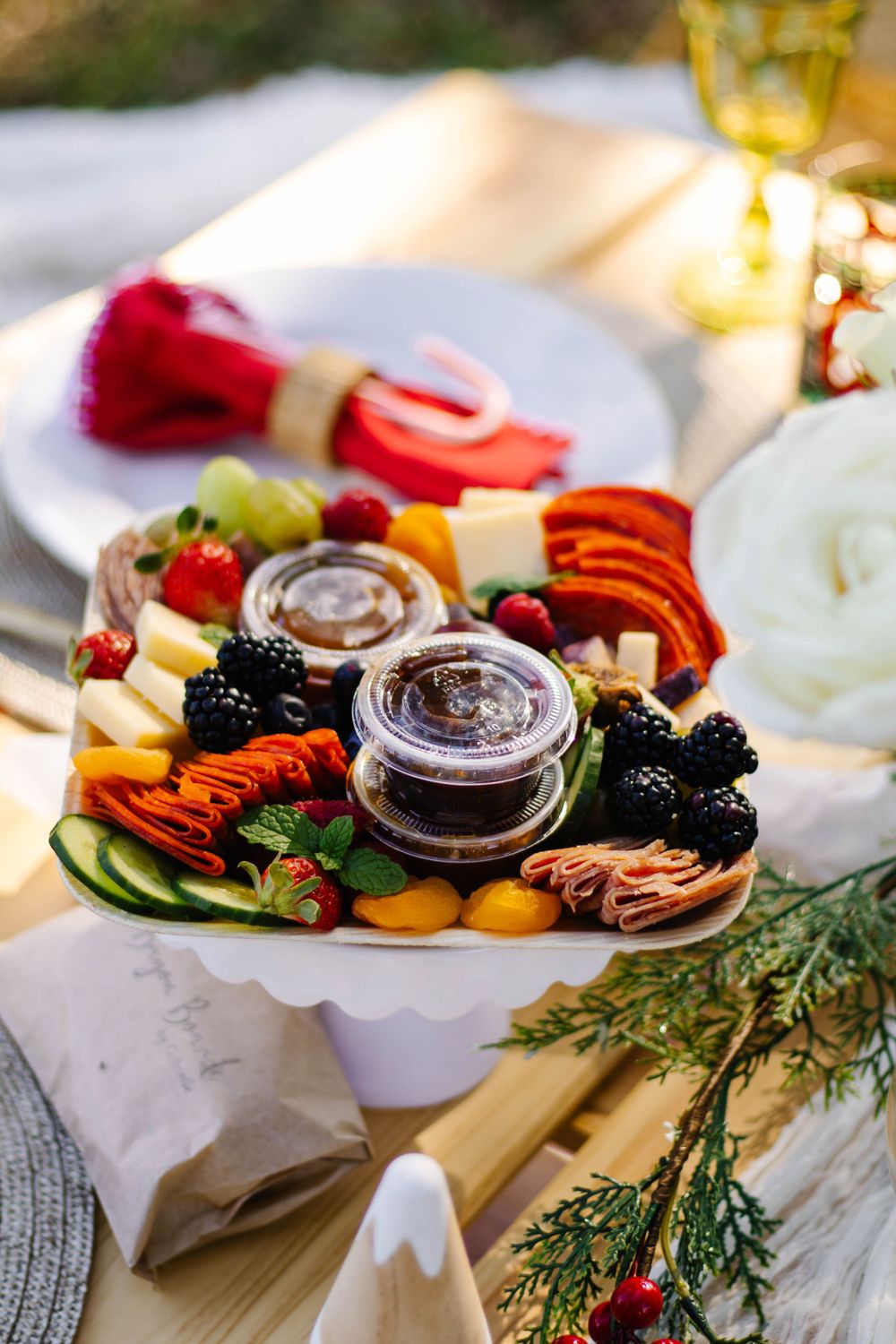 Picnic Setup artfully arranged charcuterie board with meats, cheeses, fresh berries, & two small glass jars of condiments on white platter.