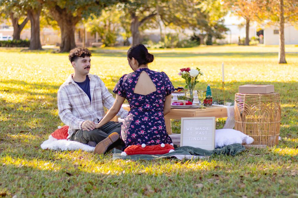 A couple enjoys a romantic autumn picnic in a park with blankets and a wicker basket under golden trees.