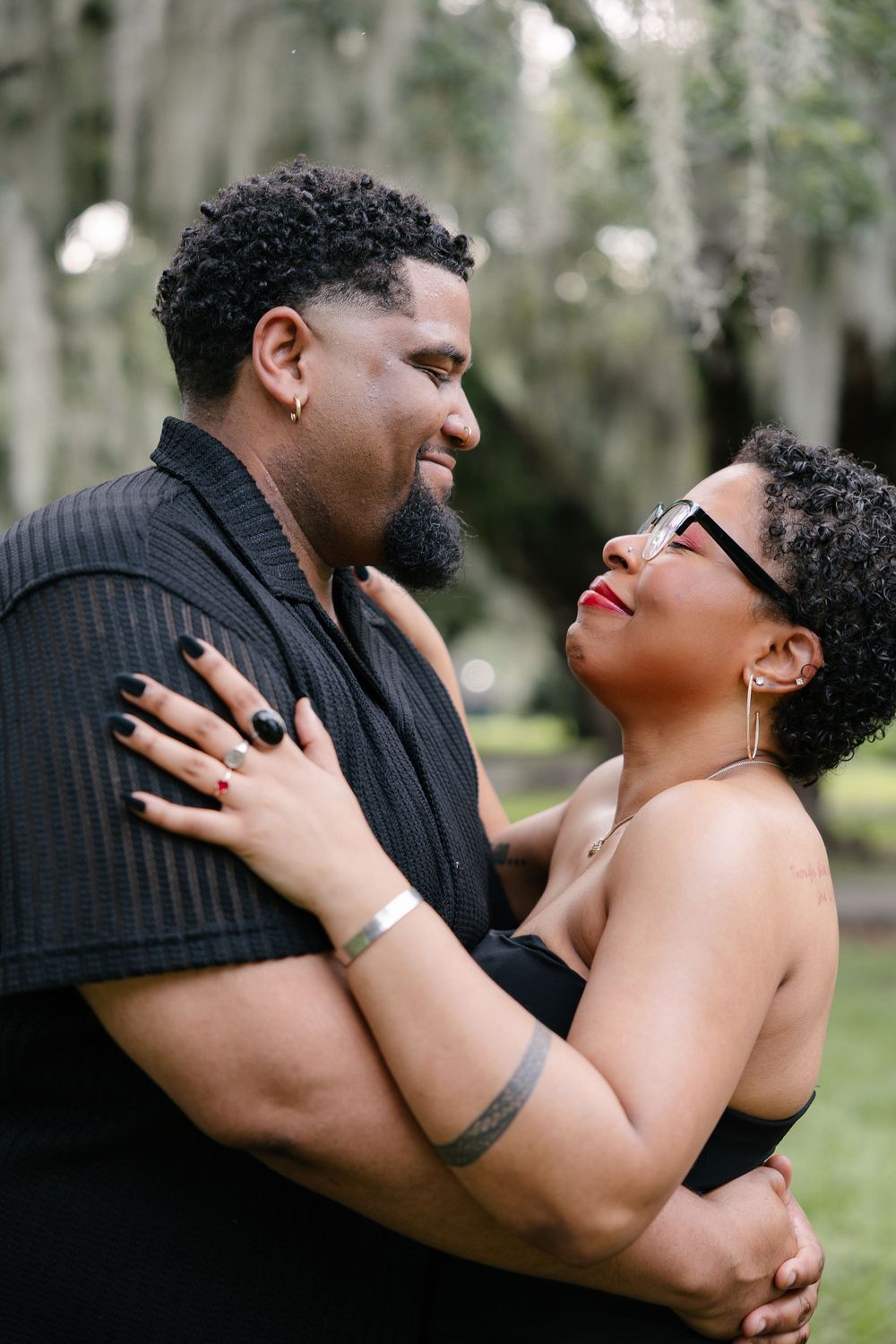 Joyful couple sharing intimate moment in outdoor setting with Spanish moss trees in background.