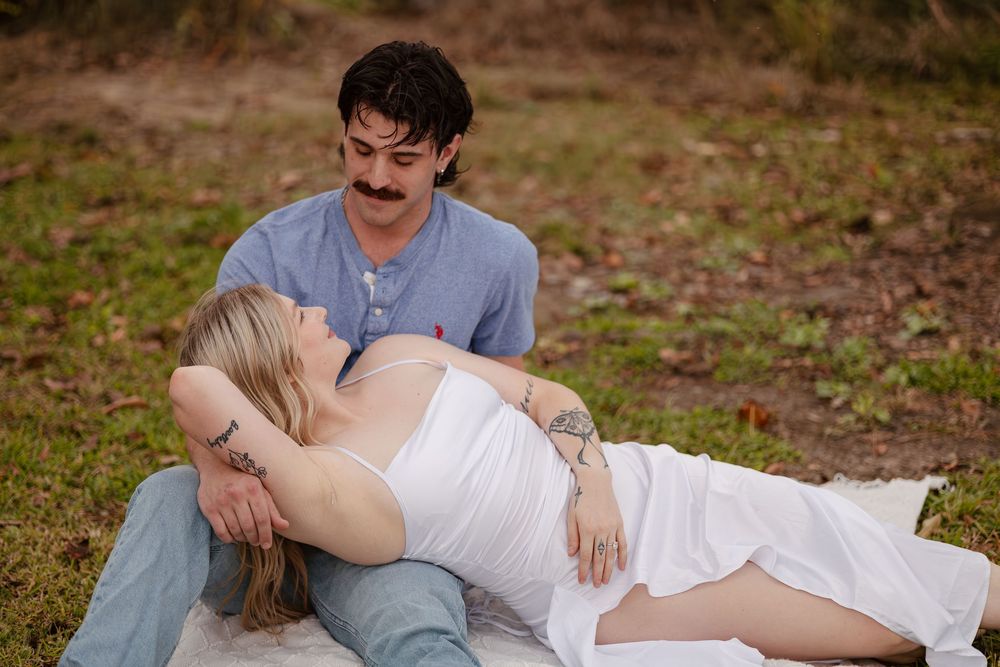 A romantic couple in formal attire poses together on fallen autumn leaves in an outdoor setting.