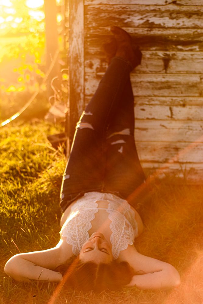 Artistic sunlit portrait on grass with golden hour lighting and rustic barn wall backdrop.