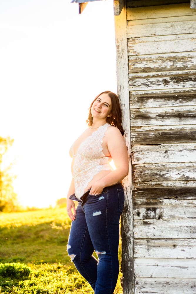 Portrait against weathered white barn wall during golden hour wearing lace top and distressed jeans.